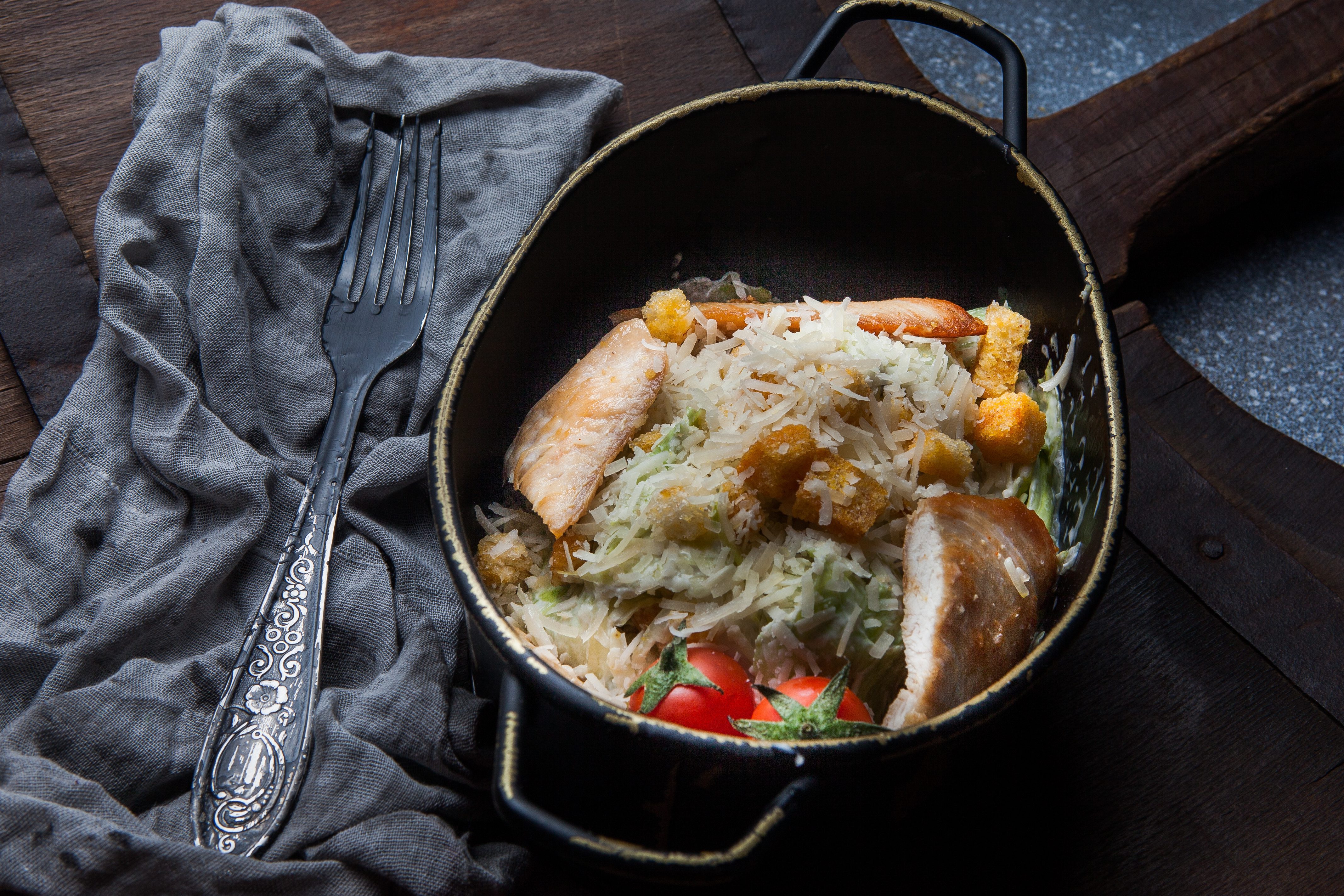 From above caesar salad with tomato and rag and fork in plate on wood background From above caesar salad with tomato and rag and fork in plate on wood background